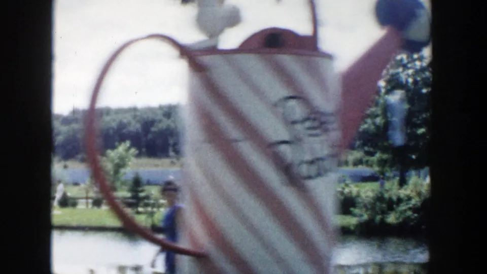 Decorative pitcher form in the foreground overlooks a landscaped Wisconsin Dells pond area with trees and tourists in the distance.