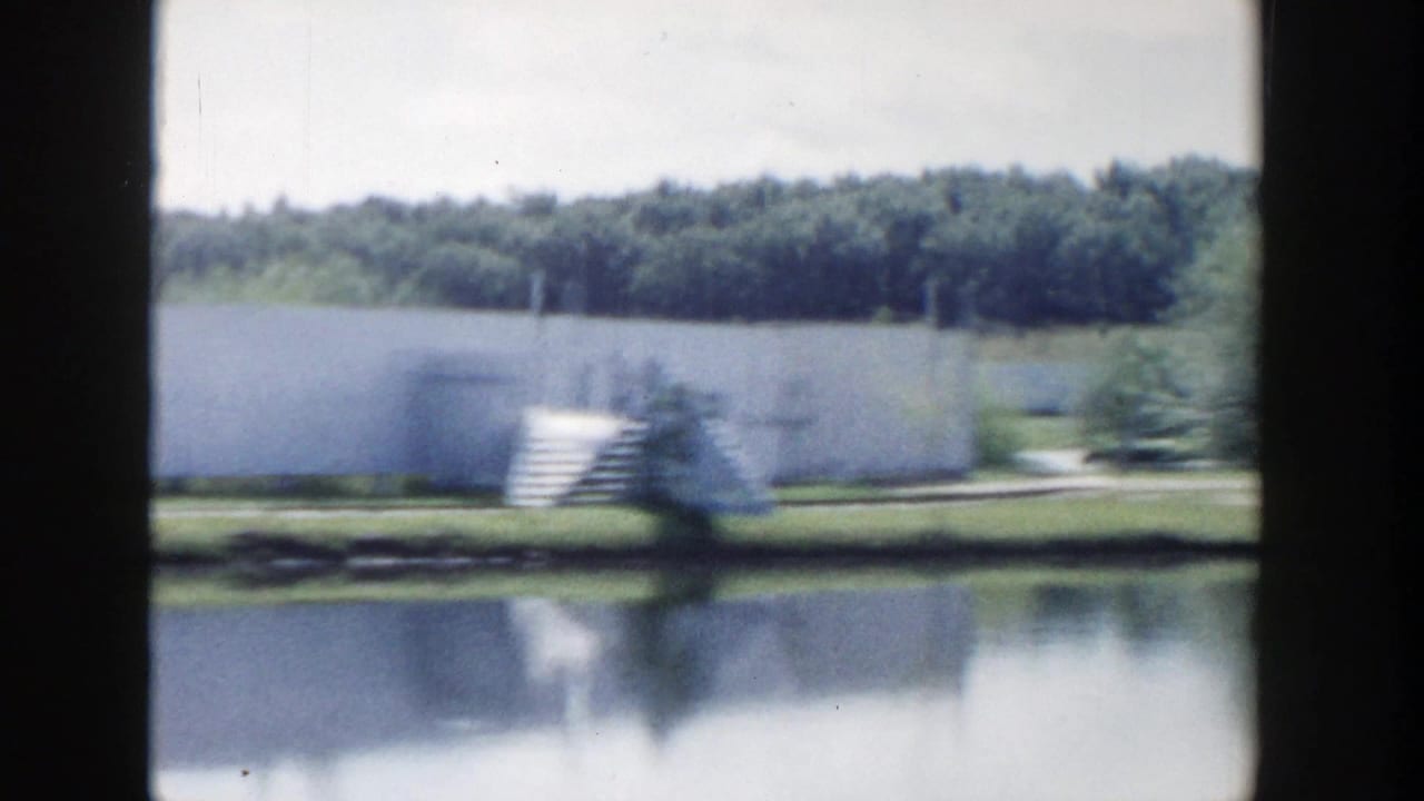 White building and lawn reflected in a pond.