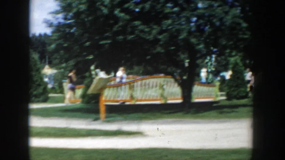 Wisconsin Dells attraction grounds with visitors near a curved bench or small ride element, framed by trees and a pale walking path.