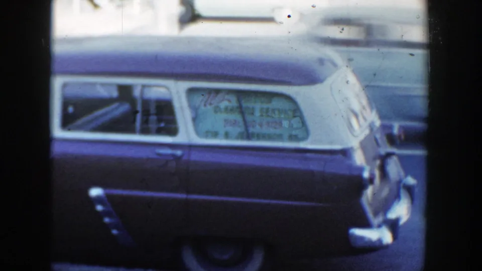 1954 Wisconsin Dells home-movie frame showing a two-tone station wagon with a window-cleaning service sign on the rear side window.