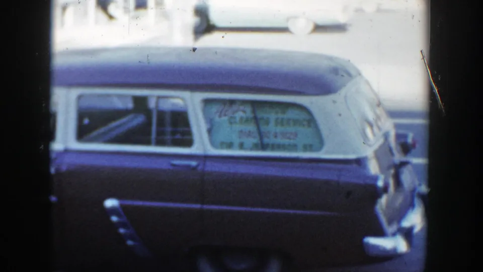 1954 Wisconsin Dells frame showing the rear half of a two-tone station wagon and visible business sign lettering in the side window.