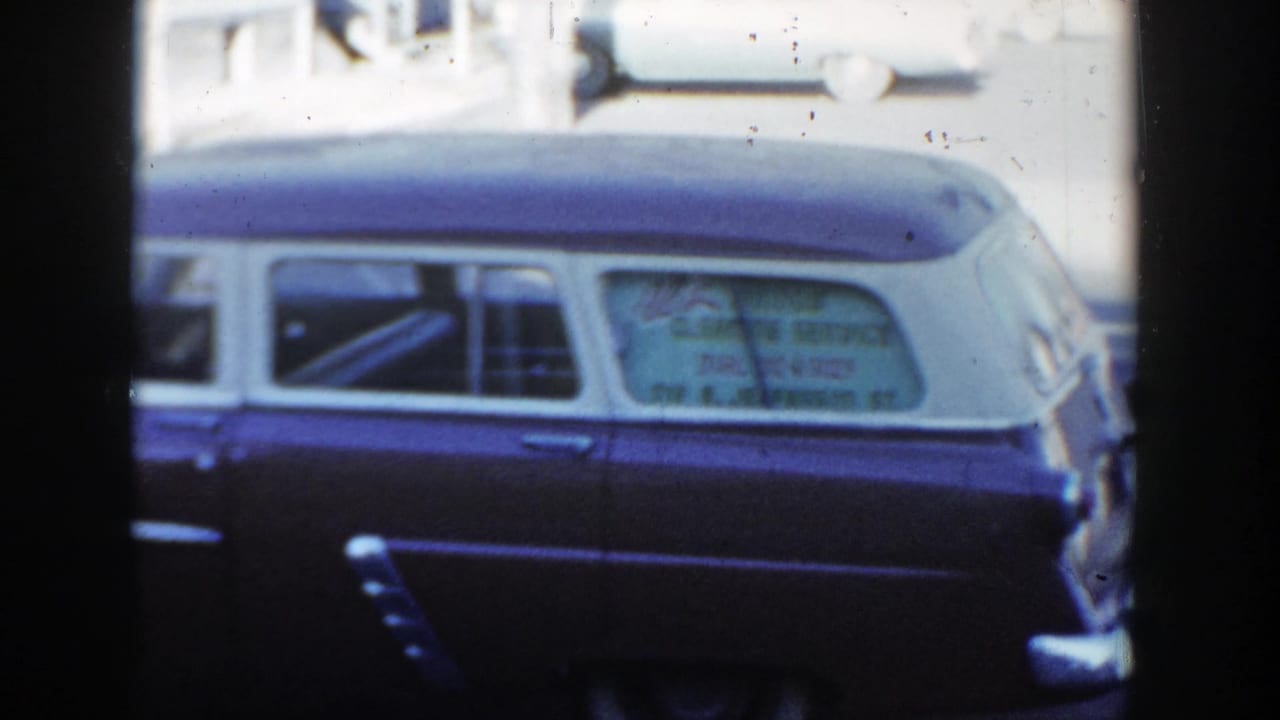 Two-tone station wagon parked beside a city street with lettering in the rear window.