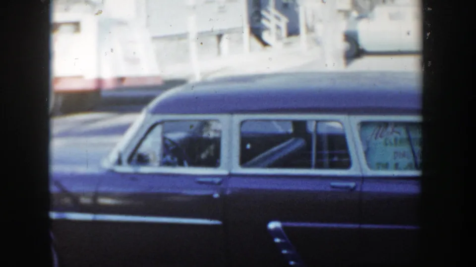 1954 home-movie frame of a two-tone station wagon along a Wisconsin Dells street, with soft-focus buildings in the background.