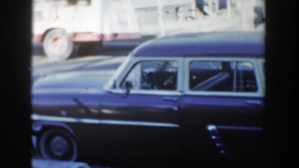 Wisconsin Dells 1954 street frame showing the front half of a dark two-tone station wagon and a passing vehicle behind it.