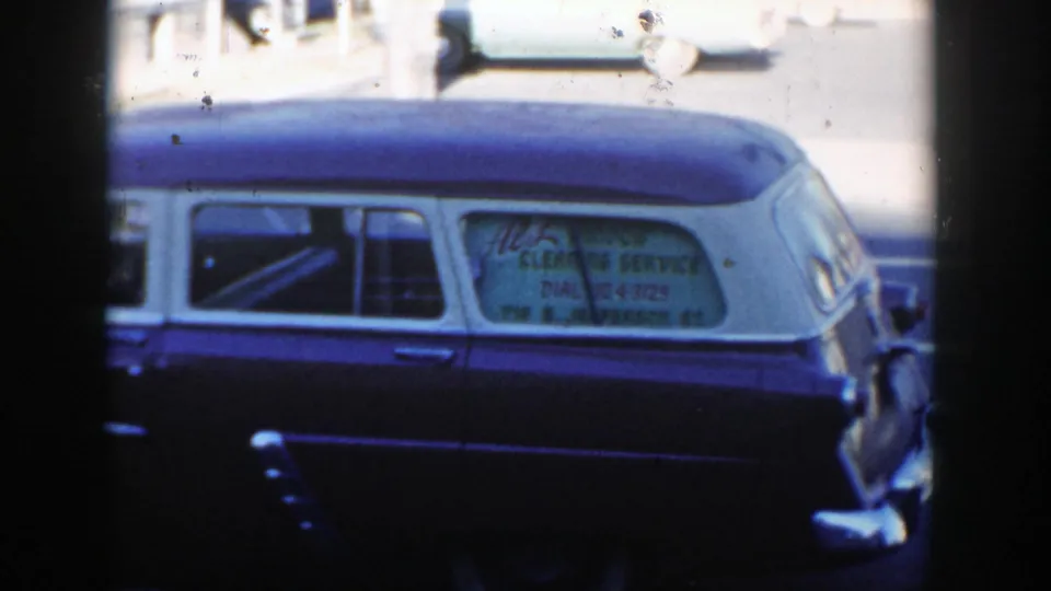 1954 Wisconsin Dells street view with a dark blue hearse-style service vehicle, white roof, and hand-lettered side window partly visible.