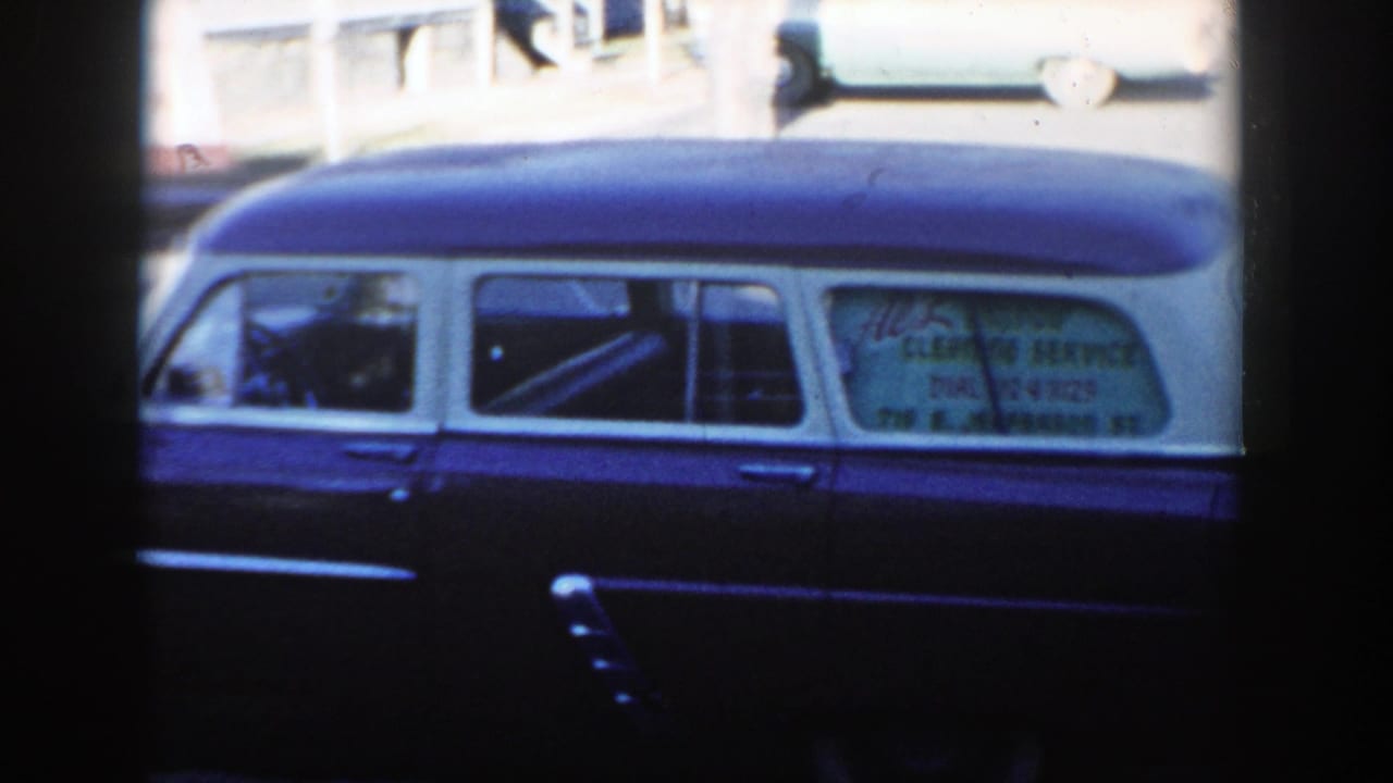 Parked two-tone vehicle with side-window lettering seen across a street.