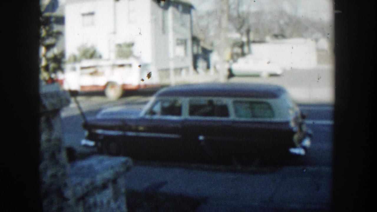 Dark station wagon with a pale roof parked along a street, seen past a dark vertical frame.
