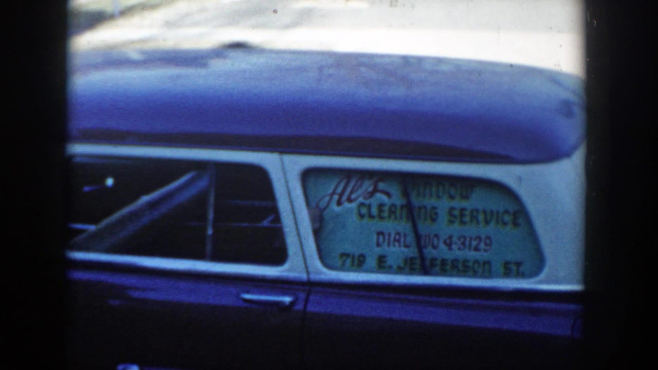 Close view of a blue-and-white station wagon with a window-cleaning service sign in the rear side window.