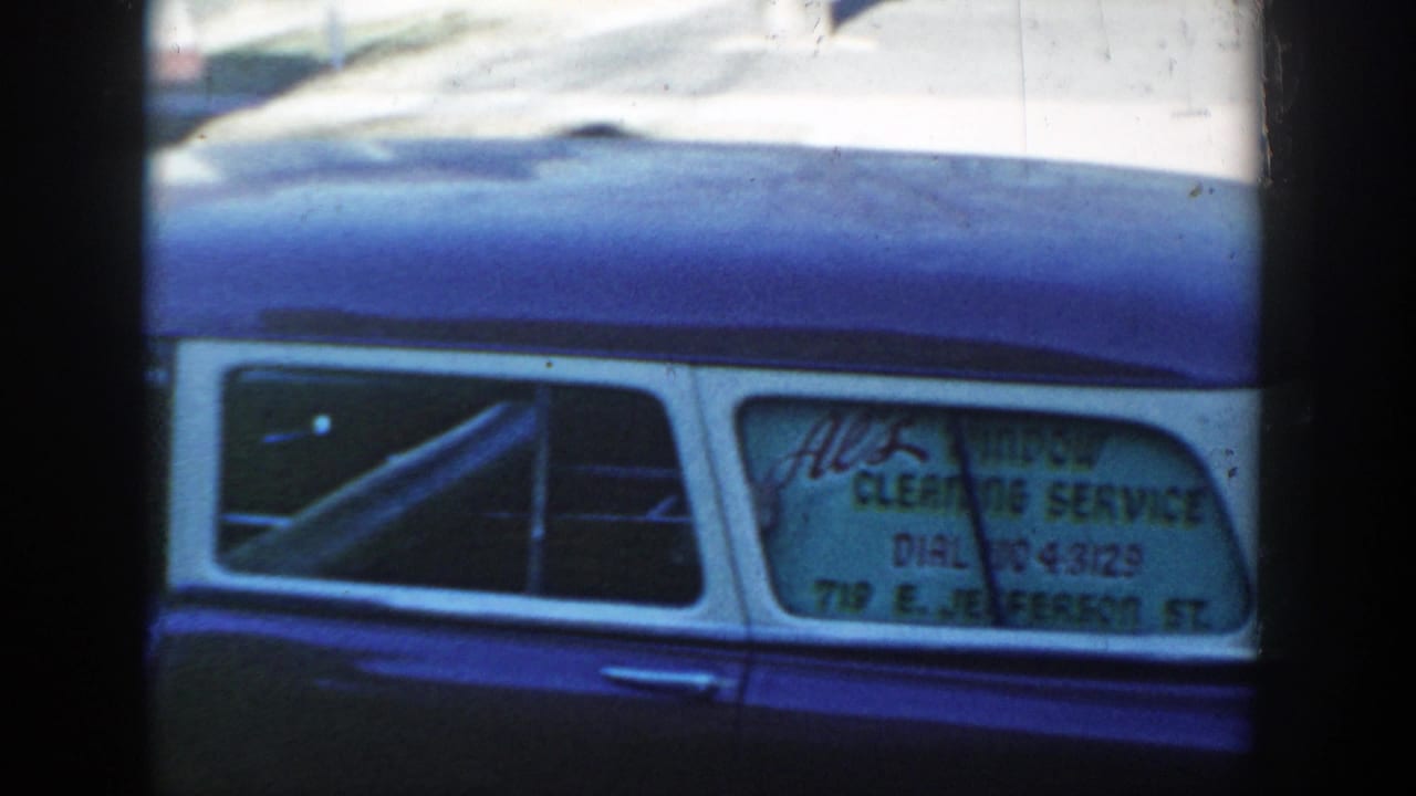 A repeated 1954 Wisconsin Dells view of the station wagon's side window, where the window-cleaning service lettering and address are partly readable.