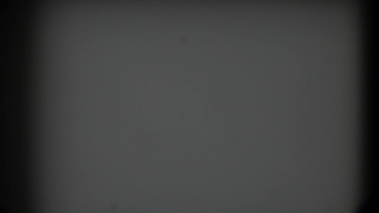1958 Texas 8mm frame with an empty gray field, dark rounded gate edges, faint grain, and scattered dust specks.