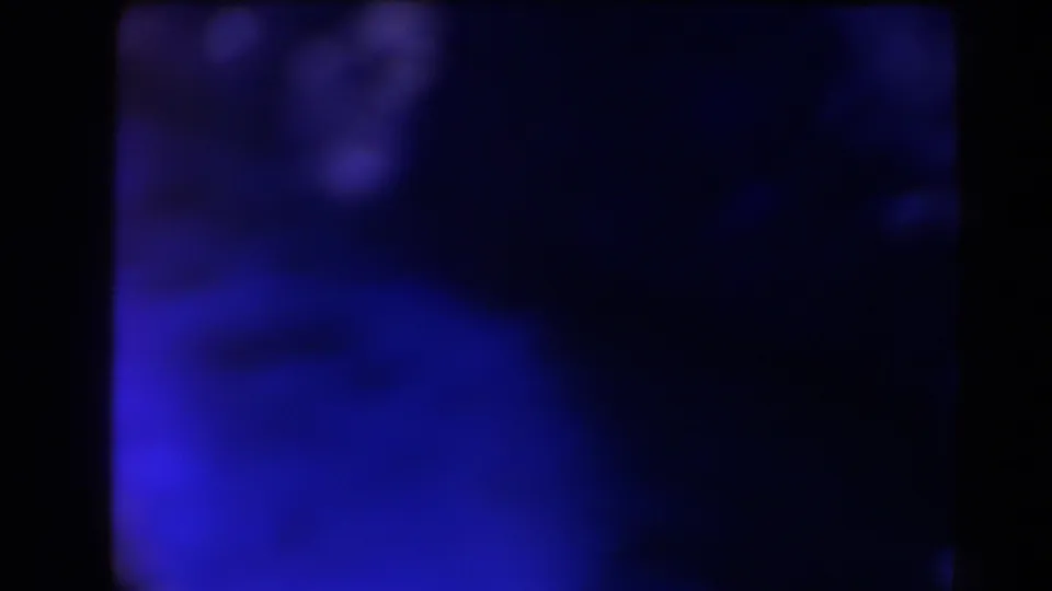 1958 Texas 8mm frame with a dark abstract view of water or shadowed rock, blue-purple tones, and grain.
