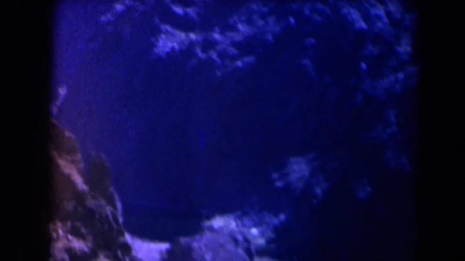 1958 Texas 8mm frame with blue-toned rock-like texture and a pale curved shoreline or beach edge in soft focus.