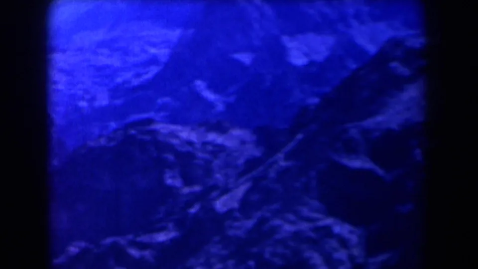 1958 Texas 8mm frame of a blue-toned rocky mountainside with shaded ridges and a possible path line.