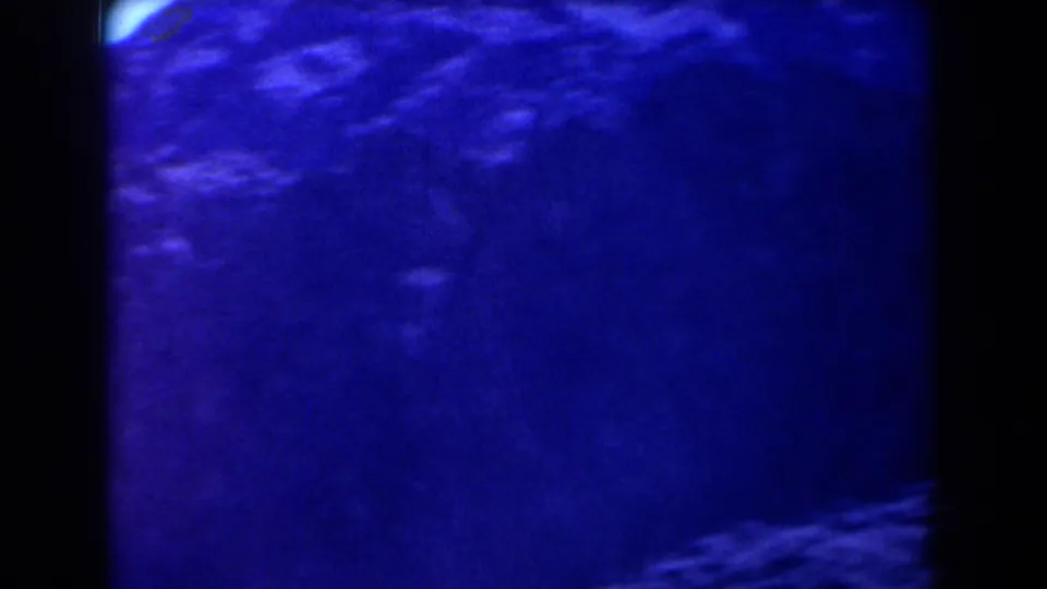 1958 Texas 8mm frame with faint shaded terrain, blue coloration, soft blur, and a small bright flare near the edge.