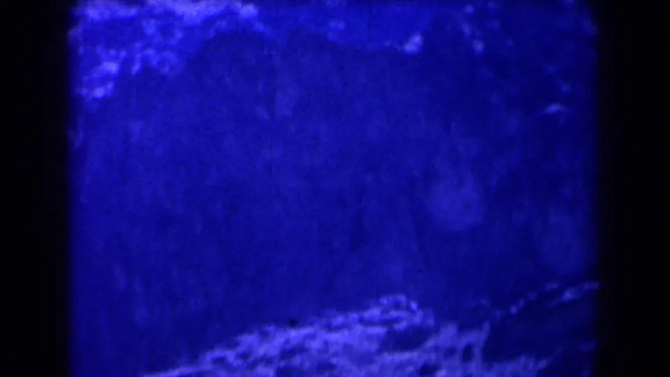 1958 Texas 8mm frame showing blue-tinted valley-like shadows, pale rocky texture, grain, and gate darkness.