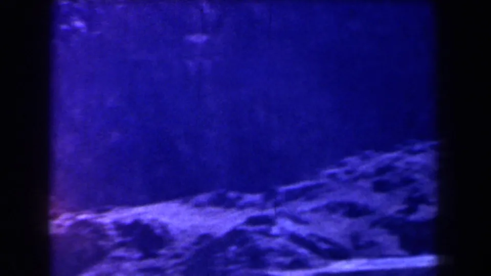 1958 Texas 8mm frame showing a blue-tinted rocky slope with soft focus, grain, and dark vertical film borders.
