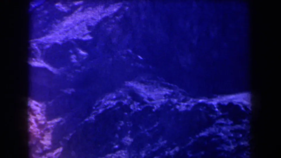 Blue-filtered 8mm view of rugged Texas rock formations divided by a dark vertical film edge or frame boundary.
