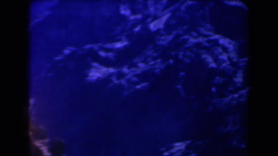 1958 Texas home-movie frame with shadowed rocky ground, strong blue tint, and soft, grainy 8mm texture.