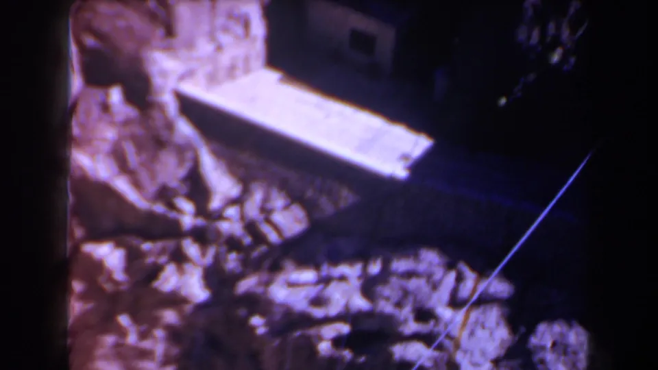 1958 Texas 8mm frame showing an angled concrete ramp or platform near rugged rock, with the tunnel area partly obscured by dark shadow.