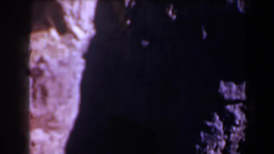 1958 Texas home-movie frame concentrating on dark shadow and rough rock texture near the tunnel opening, with little detail visible in the shade.