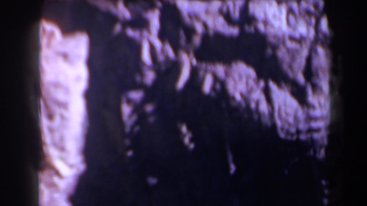Dark, grainy view of rough rock face with pale vertical stone at left.