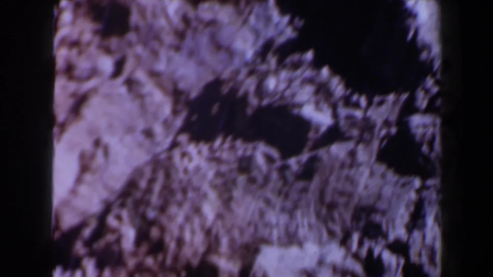 Soft, purple-toned 8mm frame of rough Texas rock formations, with dark cavities and pale stone areas visible during the pan.