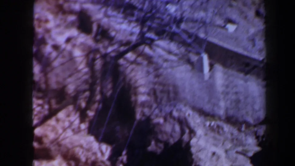 1958 8mm frame from Texas shows rugged rock below and a possible small bridge or built structure near the lower right edge.
