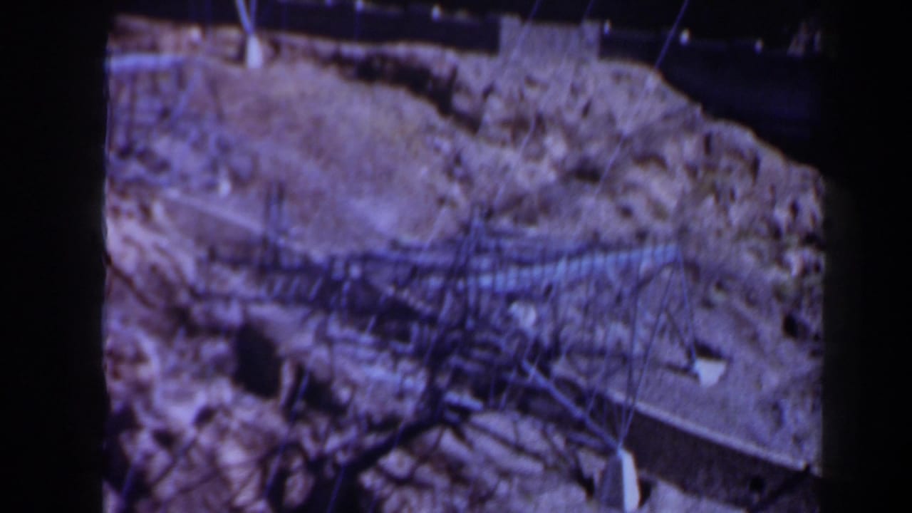 Rocky cliff face with wires and dark openings in soft 8mm footage.