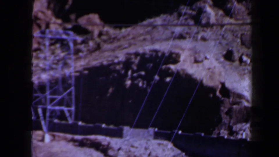 1958 Texas 8mm frame with a metal transmission tower, power lines, and a dark cut into rocky terrain.