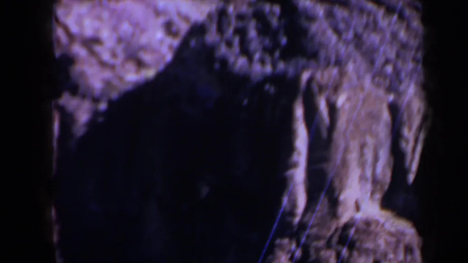 1958 Texas 8mm frame showing a close view of rough rock, a large dark recess, and vertical cliff texture.