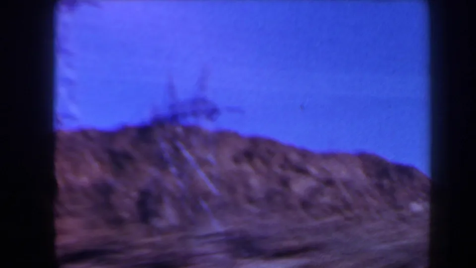1958 Texas 8mm frame showing a distant electrical tower on a rocky ridge beneath a blue sky.