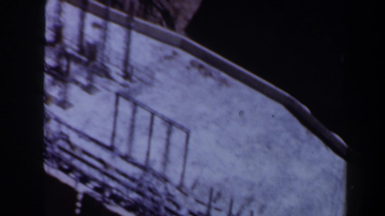 1958 Texas 8mm frame showing a pale rooftop from above, with metal posts, rail-like lines and heavy shadow around the structure.