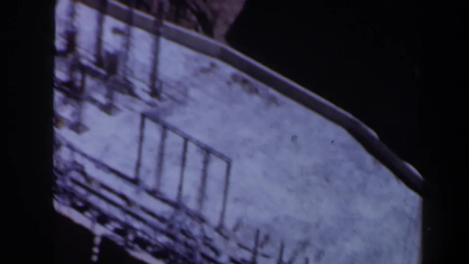 1958 Texas 8mm frame showing a pale rooftop from above, with metal posts, rail-like lines and heavy shadow around the structure.