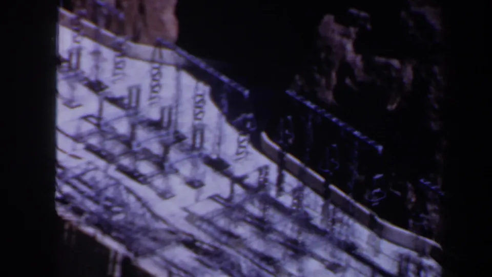 1958 Texas 8mm frame looking down across rooftop railings, repeated posts, pale concrete and a dark adjacent wall or void.