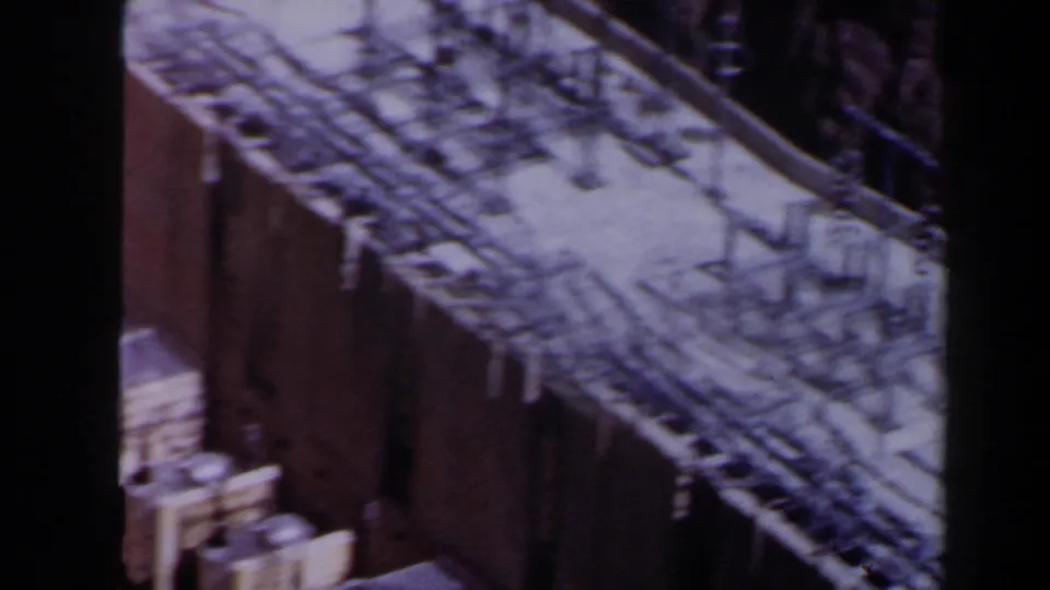 Late frame from a 1958 Texas 8mm clip showing a blurred rooftop with rows of metal fixtures and a brick or masonry wall nearby.