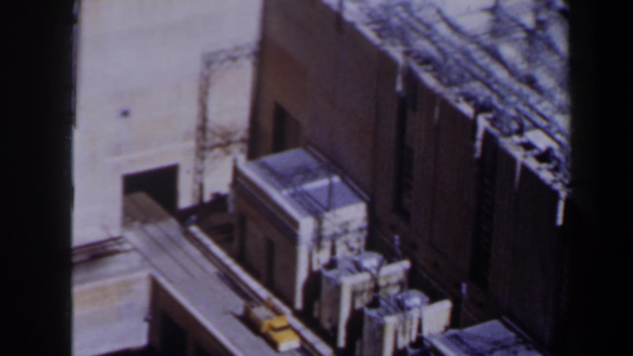 High-angle view of tan structures with dark shadows and a small yellow vehicle near an edge.