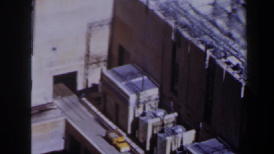 1958 Texas 8mm frame showing a high-angle view over tan building or bridge structures, heavy shadows, and a small yellow vehicle.