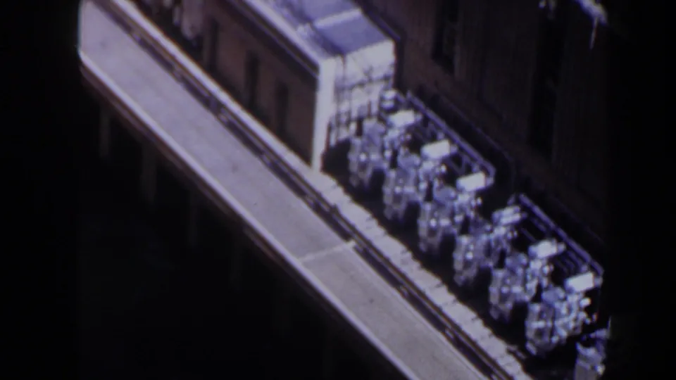 1958 Texas 8mm frame with silver cylindrical objects lined along a tan elevated structure, seen from above in bright sun.