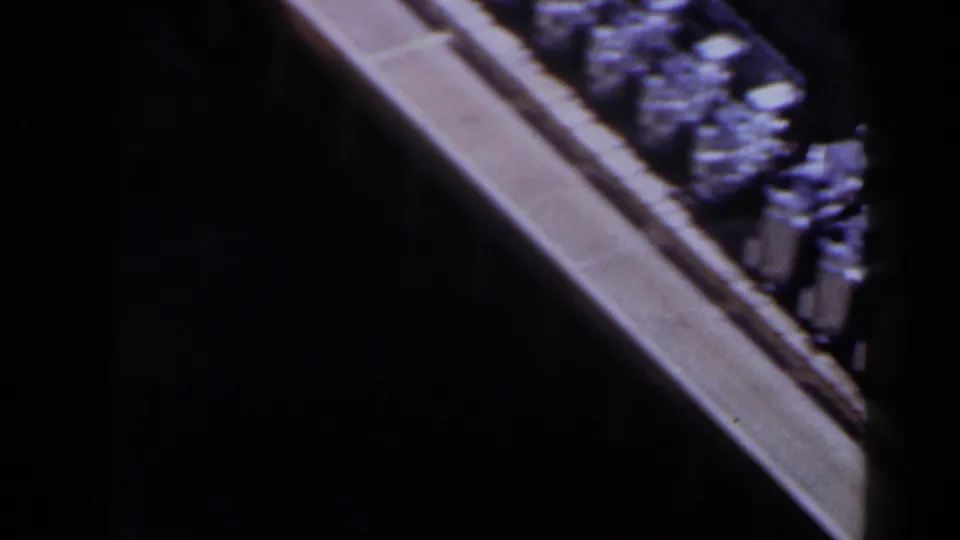 1958 Texas 8mm frame showing clustered silver objects along a tan bridge or walkway edge, with strong contrast from surrounding shadows.