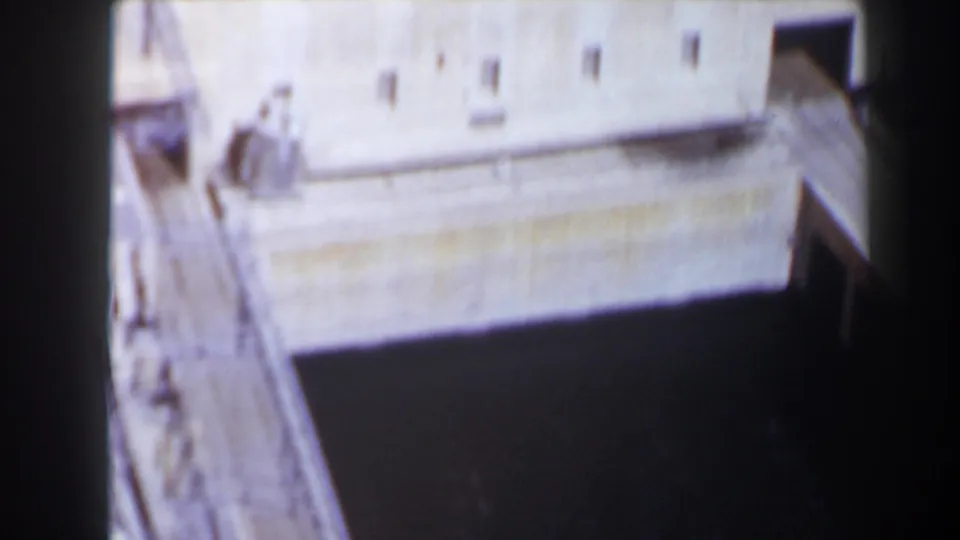 1958 Texas home-movie frame showing a close, high-angle view of the Max Starcke Dam concrete structure and dark channel below.