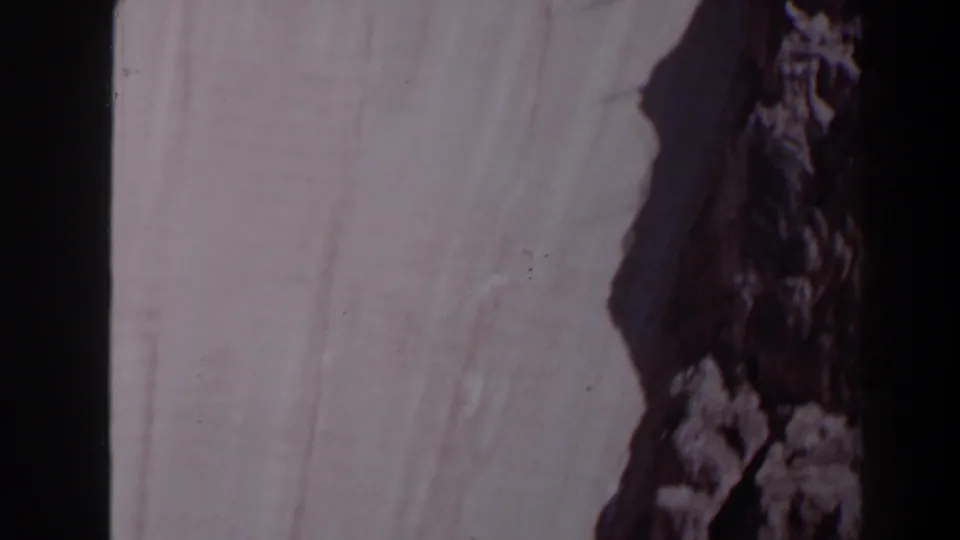 1958 Texas frame showing the Max Starcke Dam wall next to a dark rocky edge or abutment, with faded 8mm color.