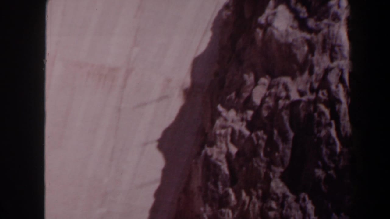 1958 Texas 8mm frame showing a concrete dam face and rugged rock formation, softened by faded color and handheld blur.