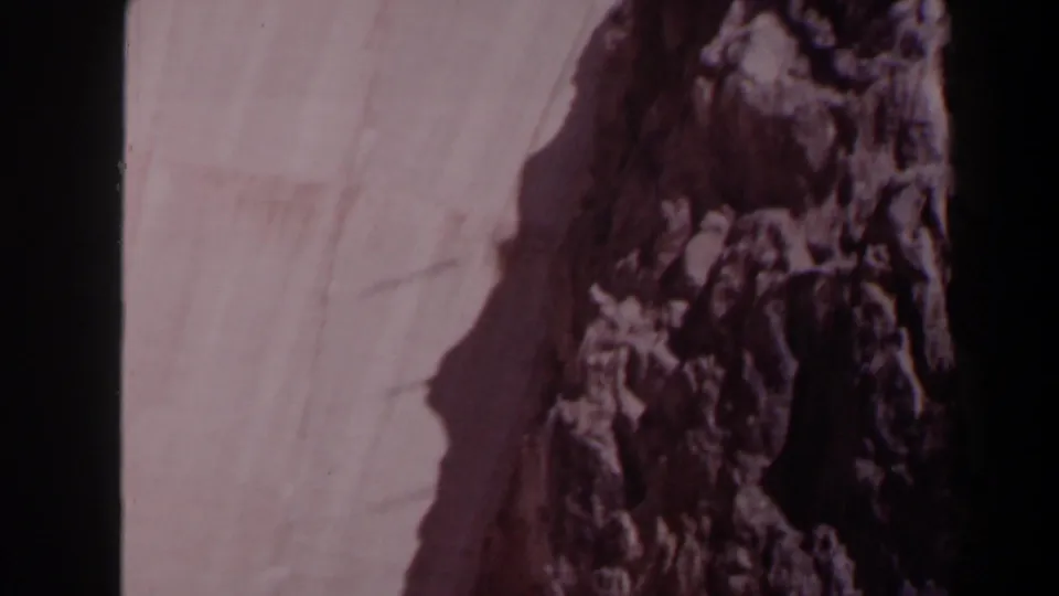 1958 Texas 8mm frame showing a concrete dam face and rugged rock formation, softened by faded color and handheld blur.