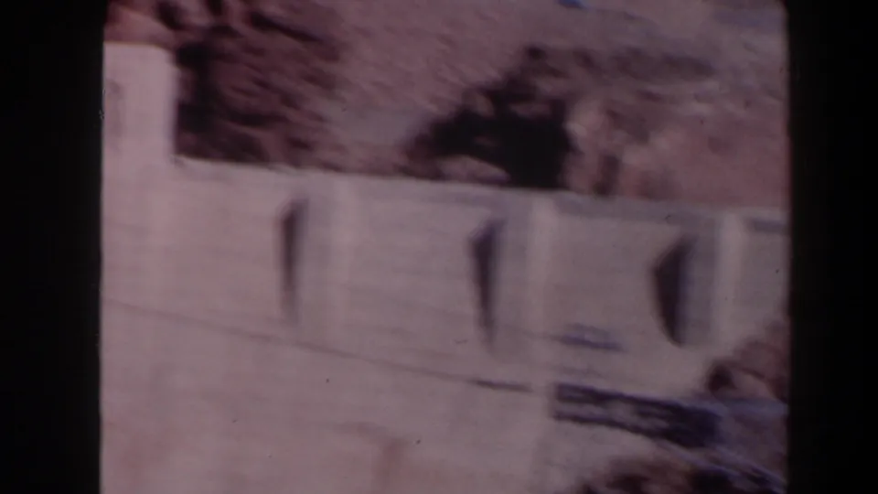 1958 Texas 8mm frame showing a blurred concrete dam section, vertical spillway-like openings, and rocky terrain above it.