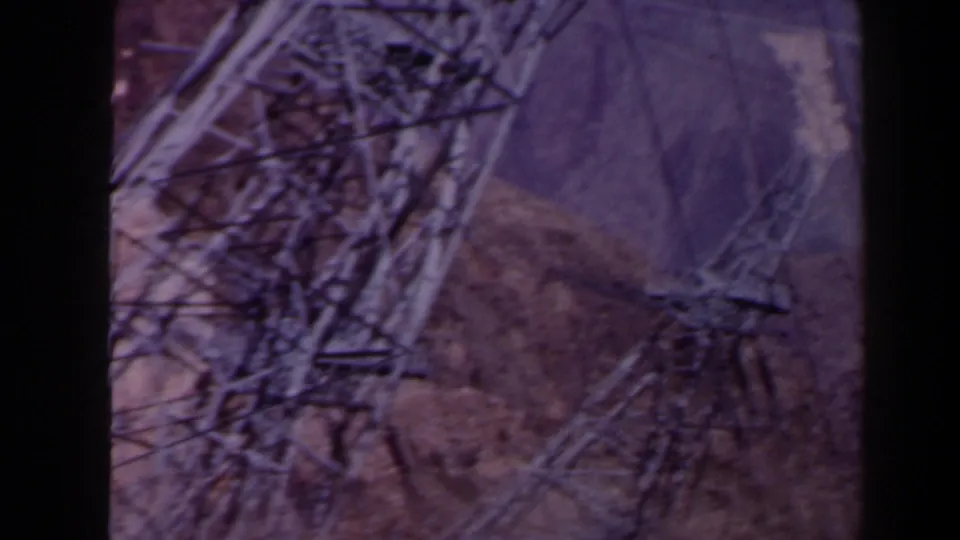 1958 Texas 8mm frame showing metal transmission towers and cables against a dam surface and rugged terrain.
