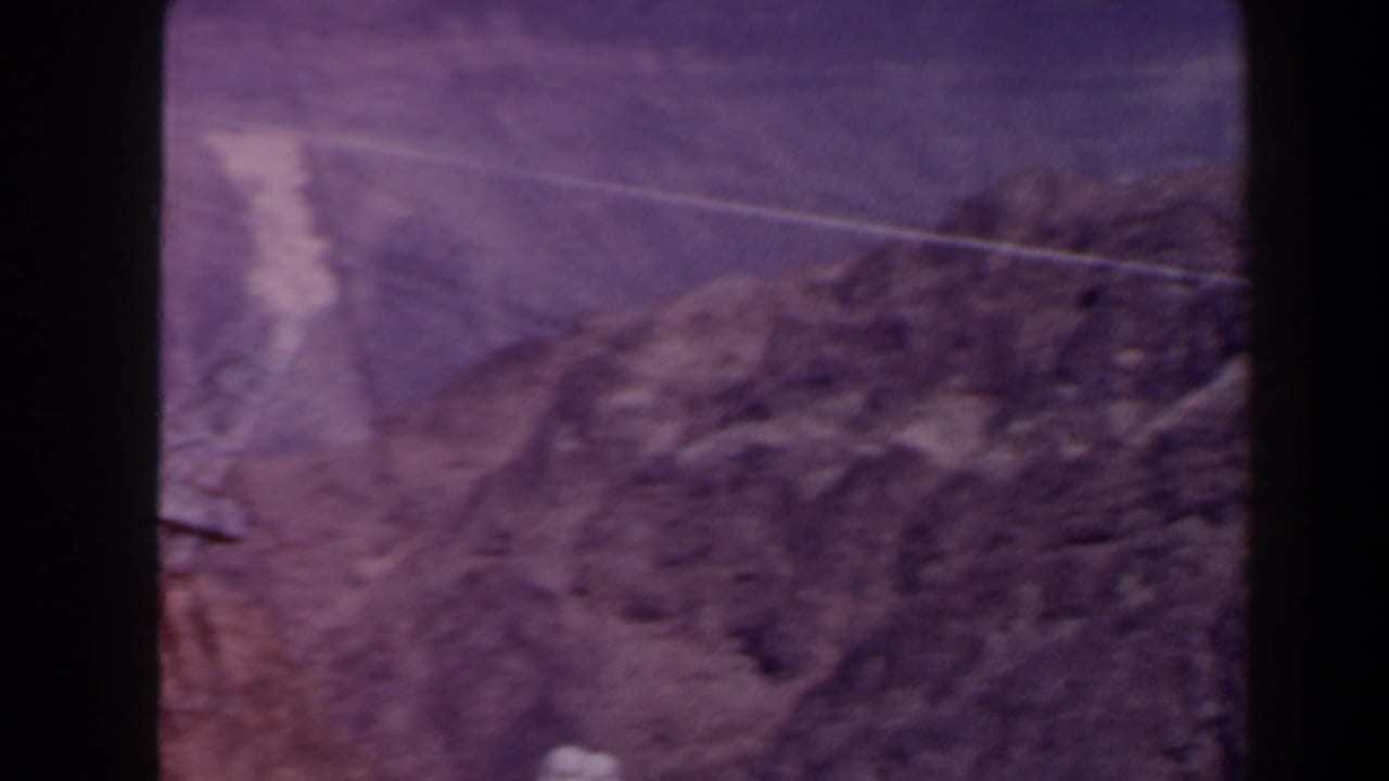1958 Texas 8mm frame showing a rocky canyon slope and a power line across arid terrain, tinted purple by aged film.