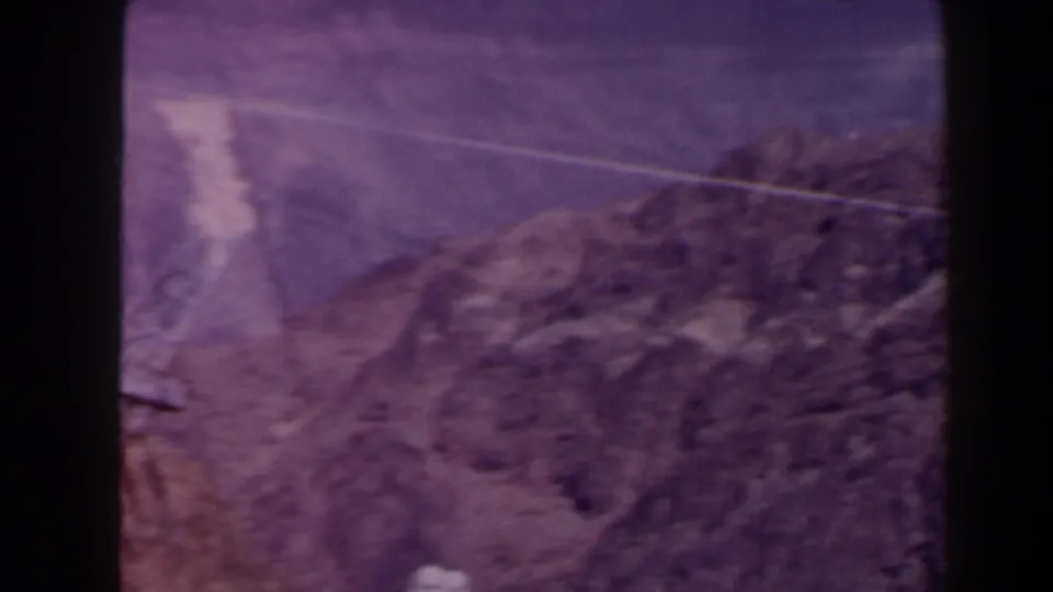 1958 Texas 8mm frame showing a rocky canyon slope and a power line across arid terrain, tinted purple by aged film.