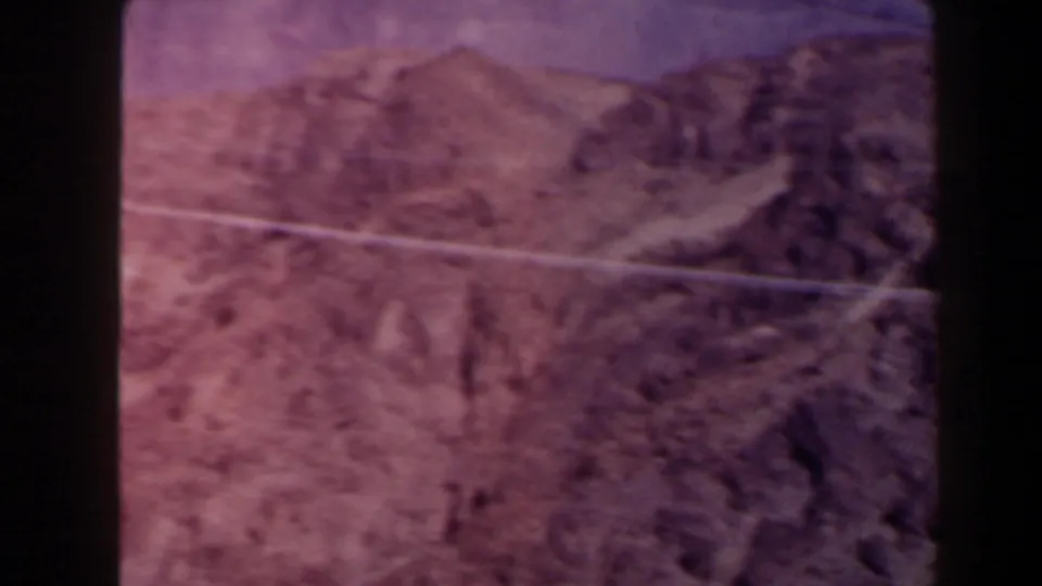 1958 Texas canyon view with rough rock faces, dry terrain, and a power line visible through the aged 8mm color cast.