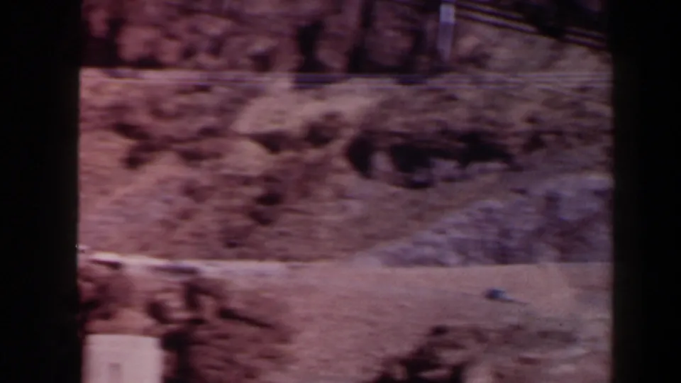 1958 Texas 8mm frame showing a canyon floor, rocky hillside, dark shadowed openings, and a pale foreground strip.
