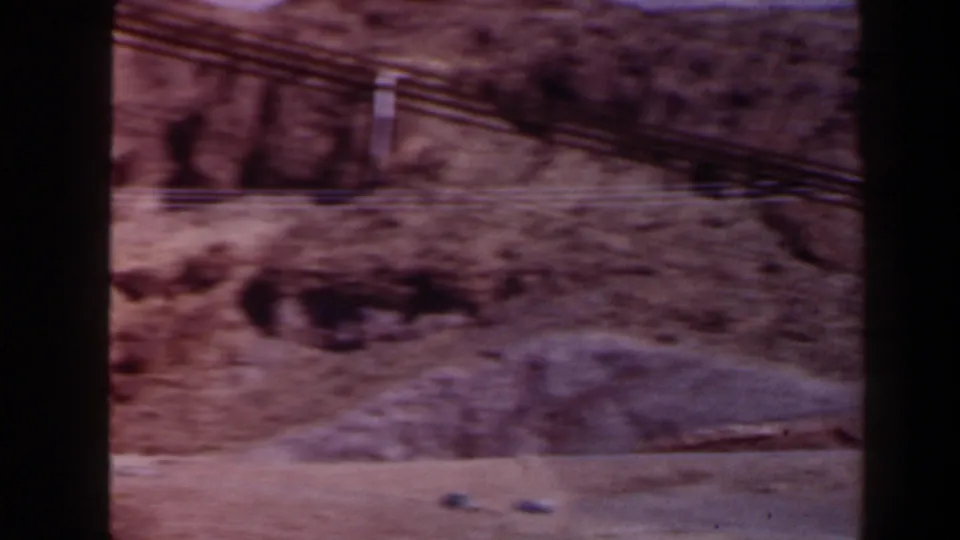 A soft 8mm view of arid Texas terrain with overhead cables, a light dirt road, and rocky slopes in faded color.